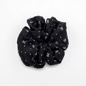 Υφασμάτινο scrunchie μαλλιών με ανάγλυφη υφή, διακοσμημένο με μικρούς φιόγκους και πουά, διαθέσιμο σε μαύρο και κρεμ χρώμα.
